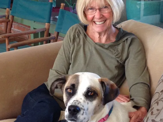 A woman with dog sitting on couch smiling