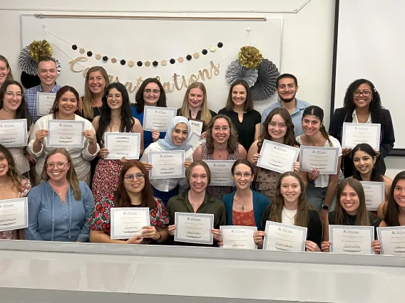 Group of individuals smiling at camera holding up certificates; congratulations banner in background