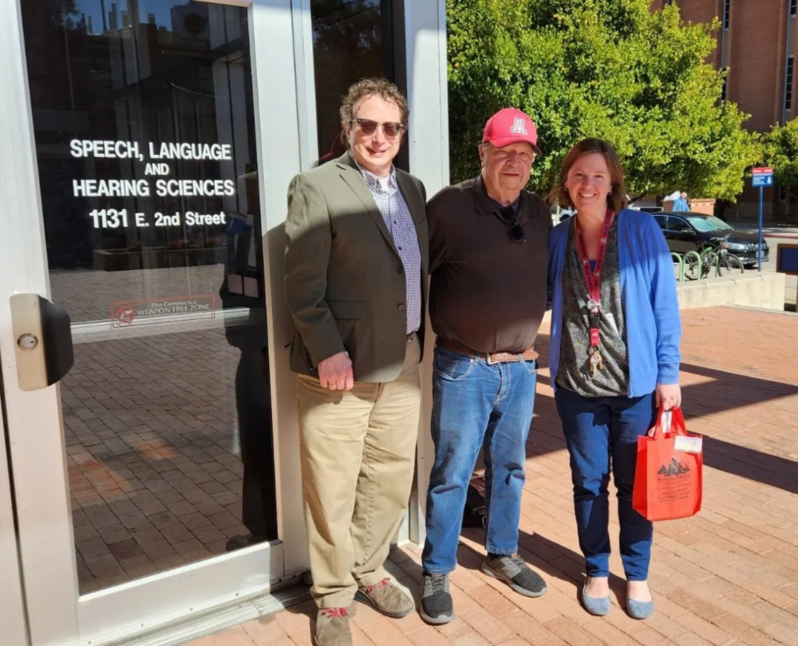 Photo of three smiling adults standing in front of glass door