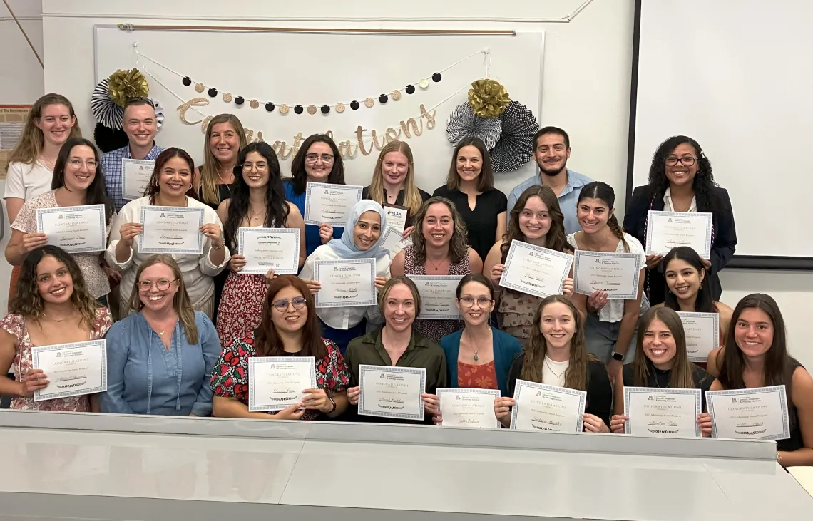 Image of large group of university students smiling at camera holding up certificates; congratulations banner in background.