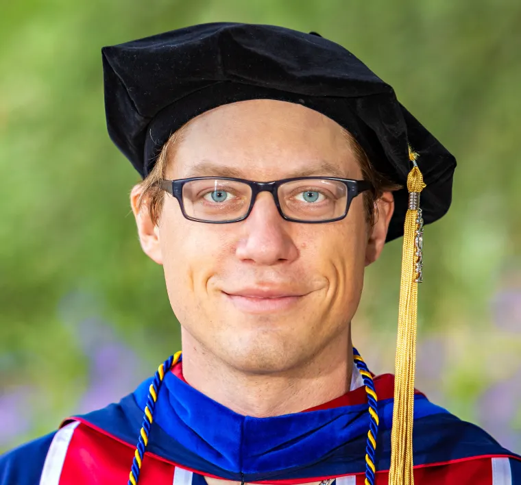 Image of man in graduation regalia smiling at camera